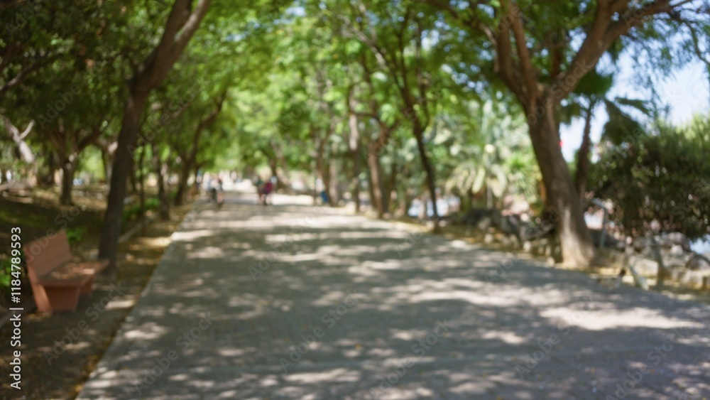 Blurred outdoor pathway with defocused trees and people walking in the background under sunlight creating bokeh effects in a park setting with shadows and greenery around Blurred outdoor pathway with defocused trees and people walking in the background under sunlight creating bokeh effects in a park setting with shadows and greenery around