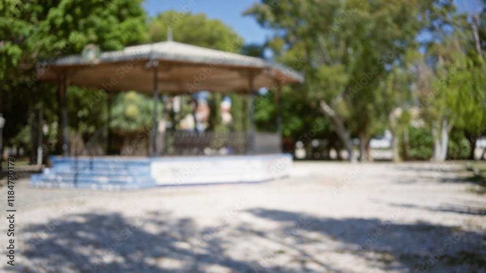 Outdoor park scene with defocused gazebo surrounded by green trees and sunny sky, blurred background highlighting bokeh effect and natural light Outdoor park scene with defocused gazebo surrounded by green trees and sunny sky, blurred background highlighting bokeh effect and natural light