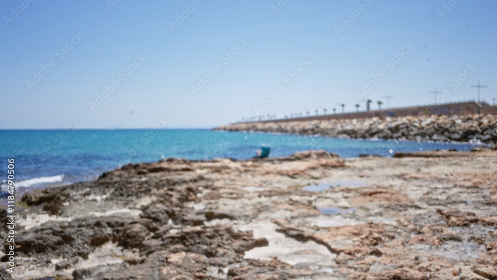 Defocused view of rocky shoreline with clear turquoise water under a blue sky Defocused view of rocky shoreline with clear turquoise water under a blue sky
