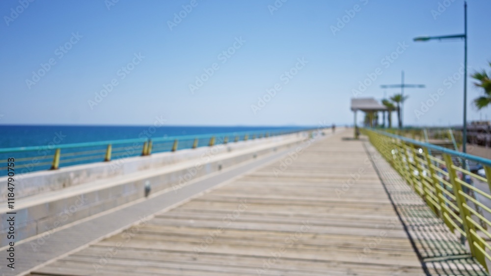 Blurred view of a wooden pier extending into the ocean, with a clear blue sky and defocused railings and street lamps, creating a tranquil seascape setting. Blurred view of a wooden pier extending into the ocean, with a clear blue sky and defocused railings and street lamps, creating a tranquil seascape setting.