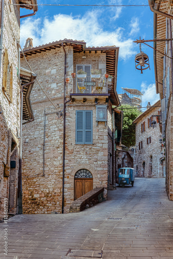 Medieval architecture and narrow streets of Assisi, traditional stone houses with balconies and a charming vintage scooter hidden in the distance.