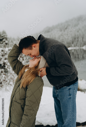 A tender young couple in a snowy valley, facing each other, the man tenderly kissing his beloved on the nose. The background is a winter forest.