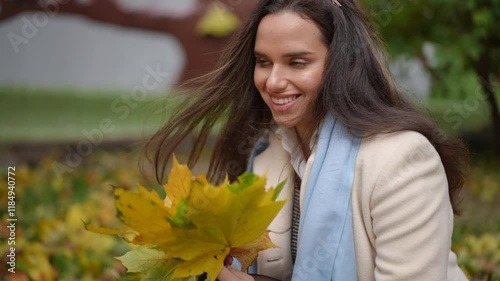 A woman enjoys autumns beauty, cheerfully holding vibrant yellow leaves in a serene naturalsetting