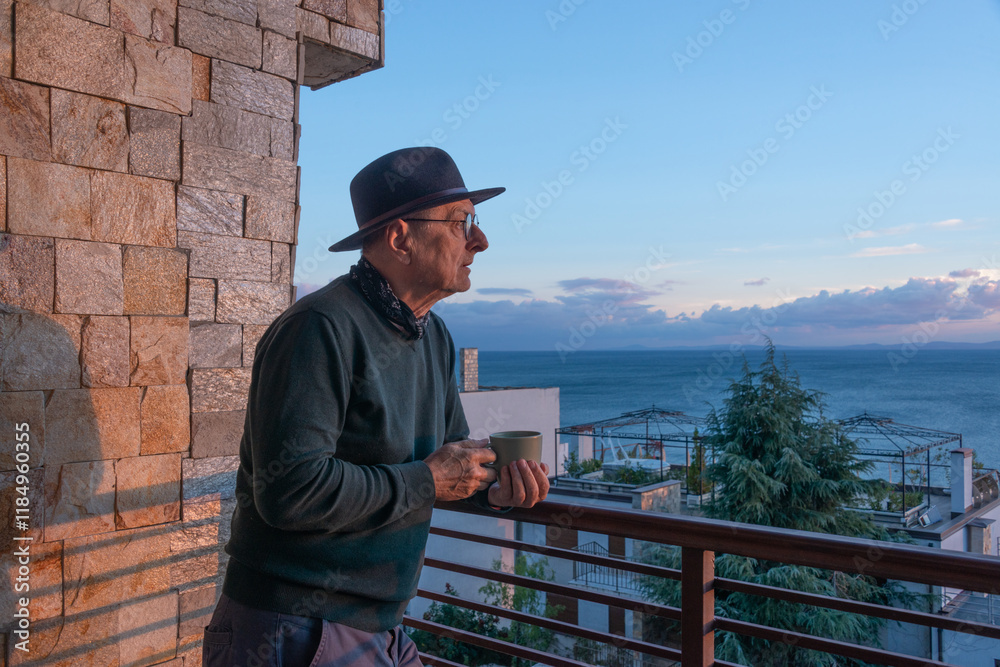 An old man enjoying cup of coffee on the balcony at sunset An old man enjoying cup of coffee on the balcony at sunset