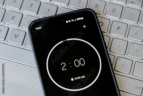A phone with a black and white 2-minute timer to study with pomodoro method on laptop keyboard, study business background