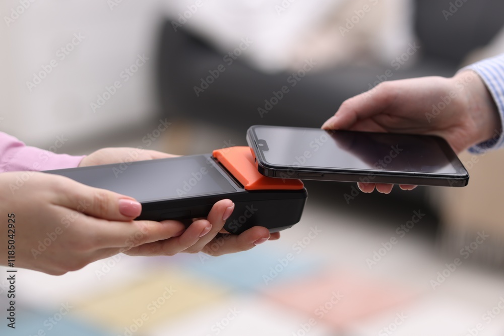 Woman paying with smartphone via terminal against blurred background, closeup Woman paying with smartphone via terminal against blurred background, closeup