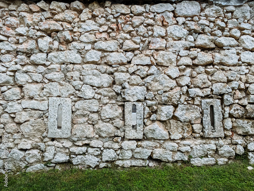 A sturdy stone wall that features a few noticeable holes within its structure, offering a glimpse into the materials used and the passage of time on this building barrier photo