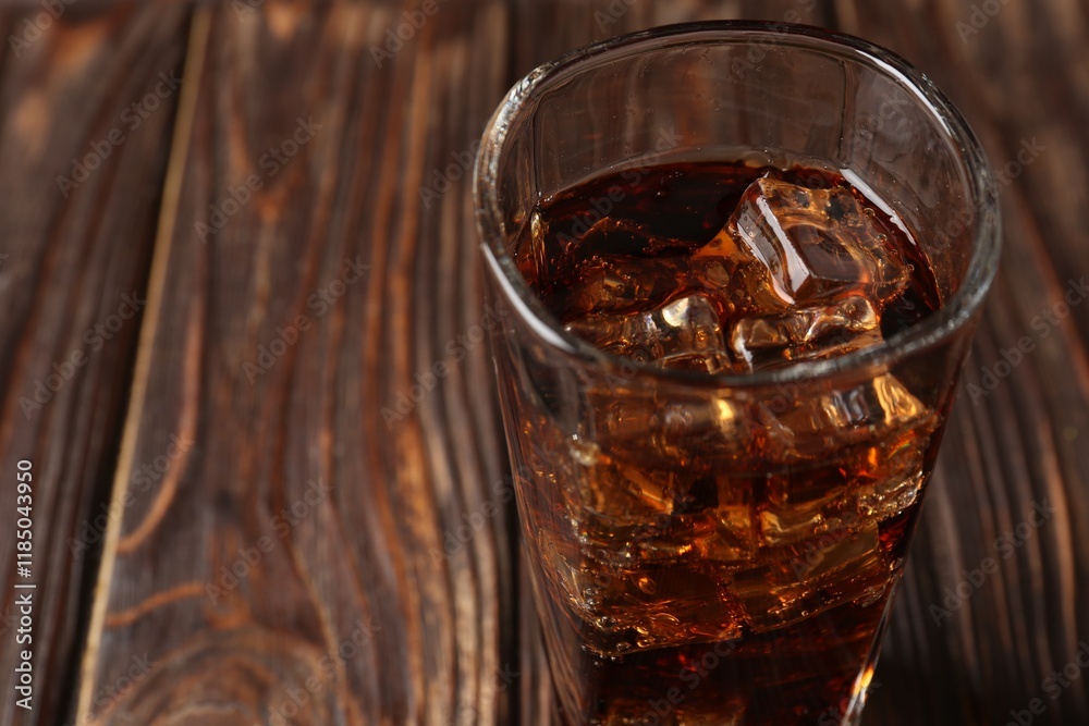 Cold cola with ice cubes in glass on wooden table, closeup. Space for text Cold cola with ice cubes in glass on wooden table, closeup. Space for text