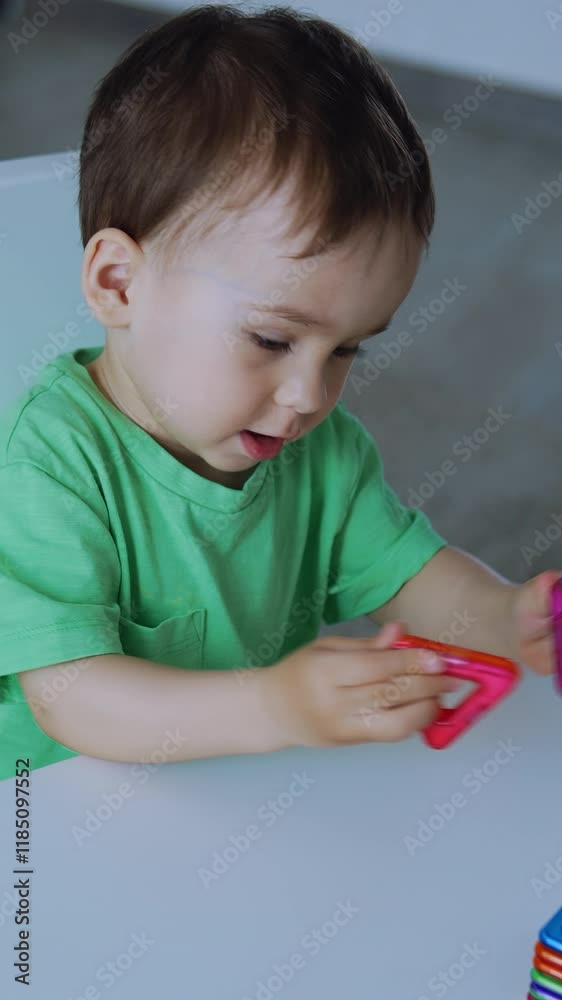 Adorable toddler plays with the toys sitting at the desk. Lovely baby learning colors and shapes. Top view. Vertical video Adorable toddler plays with the toys sitting at the desk. Lovely baby learning colors and shapes. Top view. Vertical video