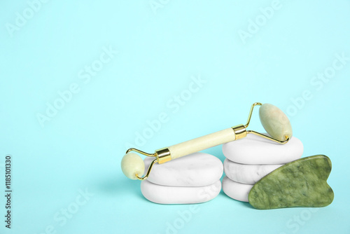 Face roller, gua sha tool and massage stones on light blue background. Space for text photo