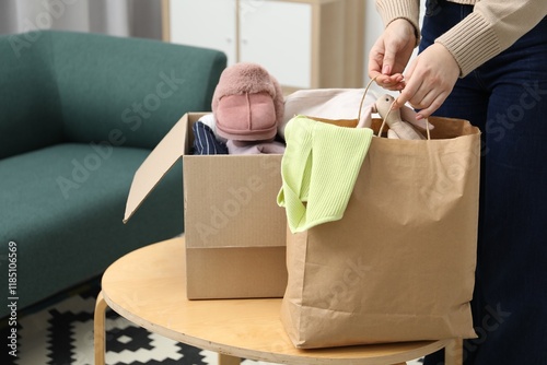 Woman with paper bag and box of used clothes at coffee table indoors, closeup photo