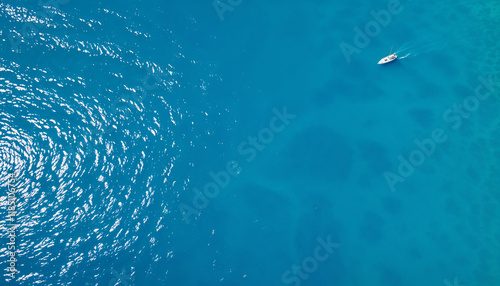 Aerial view of a serene turquoise sea with shimmering sunlight reflections and a solitary boat in the distance, perfect for tropical and aquatic themes photo