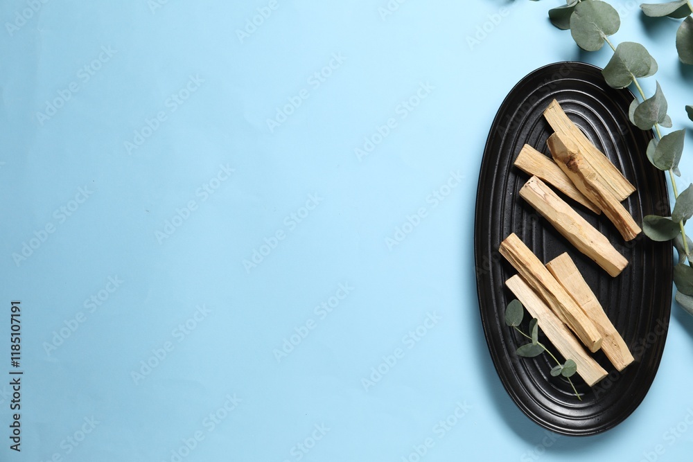 Fototapeta premium Palo santo sticks and eucalyptus branches on light blue background, flat lay. Space for text