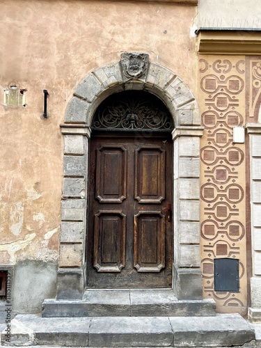 Antique wooden door with an arched stone frame  decorated with a carved metal pattern. Facade with an aging effect and decorative elements. Historical architecture.