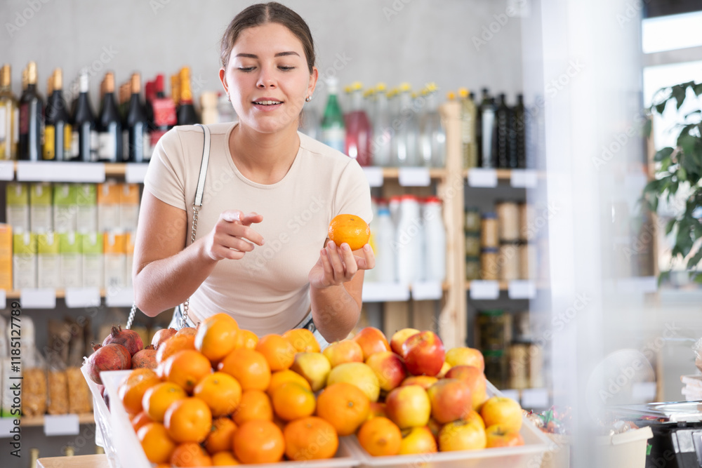 Dark-haired girl buys tangerine in store. She takes ripe fruits out of display case, inspects goods and buys tangerine . She picks ripe fruits from large box in stores storage Dark-haired girl buys tangerine in store. She takes ripe fruits out of display case, inspects goods and buys tangerine . She picks ripe fruits from large box in stores storage