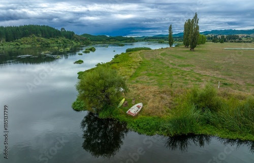 Tranquil river scene. Small rowboat rests on the grassy bank. Peaceful landscape with hay bales in the background. LAKE ANIWHENUA, MURUPARA, BAY OF PLENTY, NEW ZEALAND photo