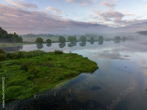 Misty morning on a tranquil lake. Birds glide across the water's surface, reflecting the soft sky. Peaceful rural scene. LAKE ANIWHENUA, MURUPARA, BAY OF PLENTY, NEW ZEALAND photo