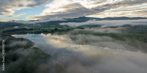 Misty morning over a tranquil lake. Reflections of clouds on still water. Peaceful rural landscape. LAKE ANIWHENUA, MURUPARA, BAY OF PLENTY, NEW ZEALAND