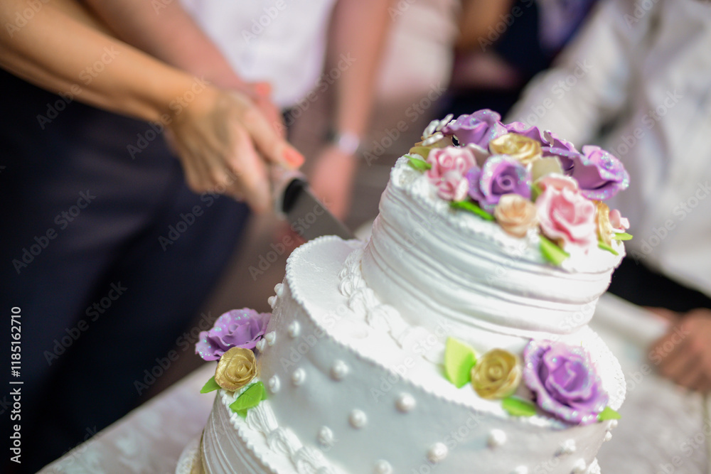 Cutting Three-tiered wedding cake with gold ribbon and bow and decorative flowers and has a white base with beads Cutting Three-tiered wedding cake with gold ribbon and bow and decorative flowers and has a white base with beads