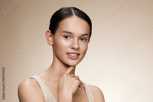 Beautiful young woman with natural makeup and neutral background, showcasing clear skin, graceful pose, and a confident smile, reflecting beauty and self care photo