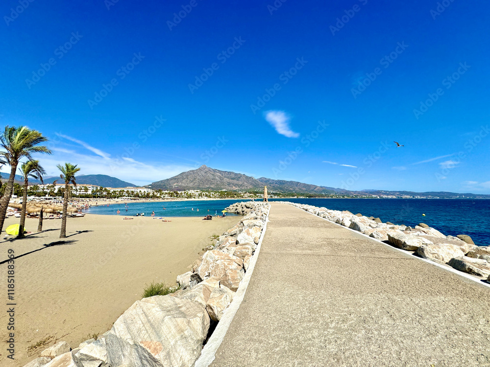 Fototapeta premium Playa Puerto Banús beach with palms and a view towards the Pico de la Concha mountain seen from the view from the harbor wall, landmark of Marbella, Malaga, Costa del Sol, Spain