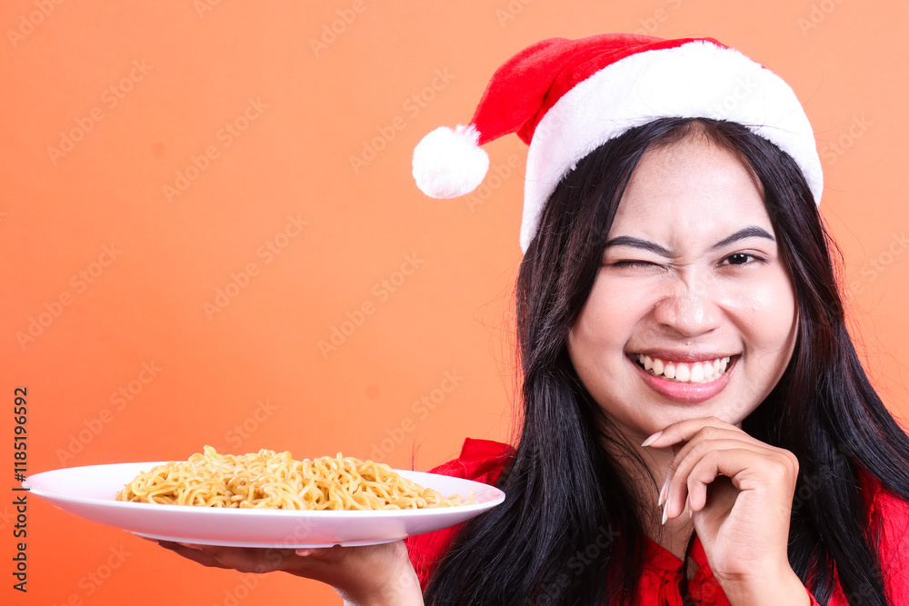 close up expression of adult ladies wearing christmas dress, Santa hat, winking smile to camera, hand holding white plate filled with noodles to the side and chin, isolated on orange background close up expression of adult ladies wearing christmas dress, Santa hat, winking smile to camera, hand holding white plate filled with noodles to the side and chin, isolated on orange background