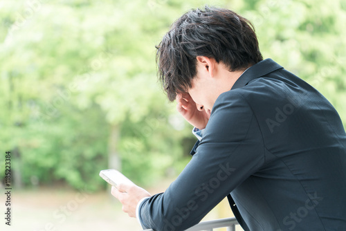 スマホを見ながら悩むビジネスマン（考える・退職・リストラ・パワハラ・プレッシャー・ストレス）
 photo