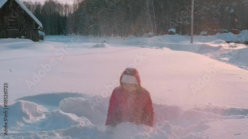 Girl in red winter coat in snowdrift having fun throwing snow on frosty day. Countryside on background. High quality 4k footage photo