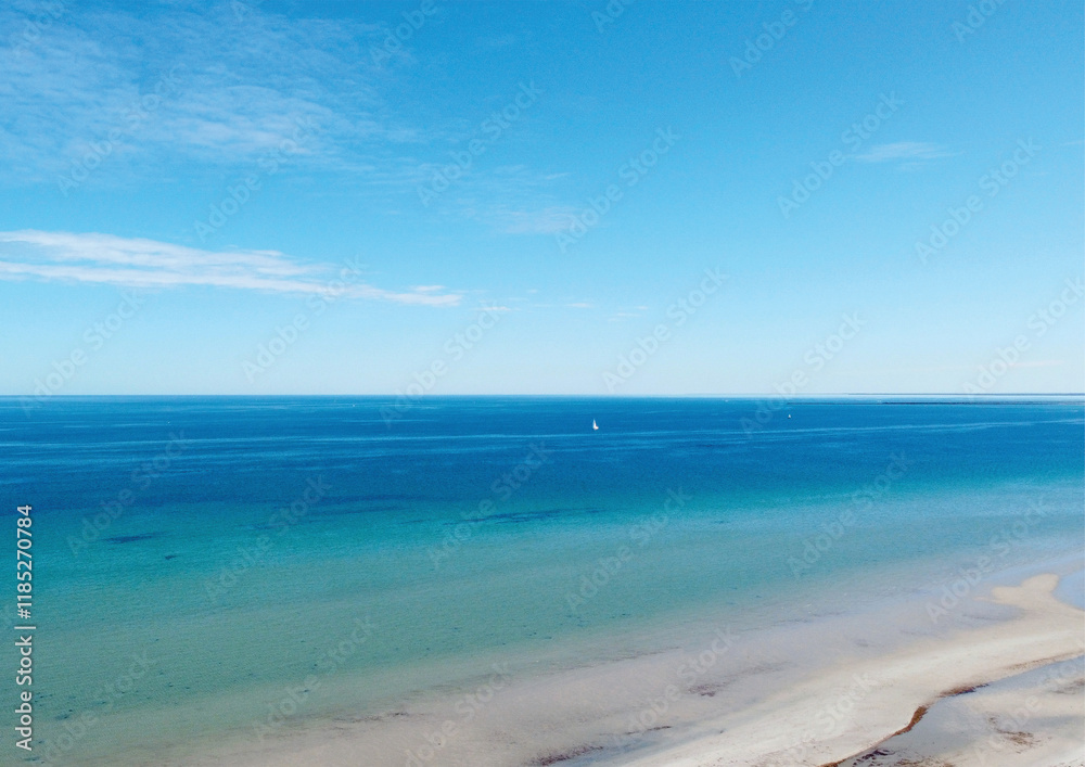 Aerial view of calm ocean waves under a vibrant blue sky with a distant sailboat Aerial view of calm ocean waves under a vibrant blue sky with a distant sailboat