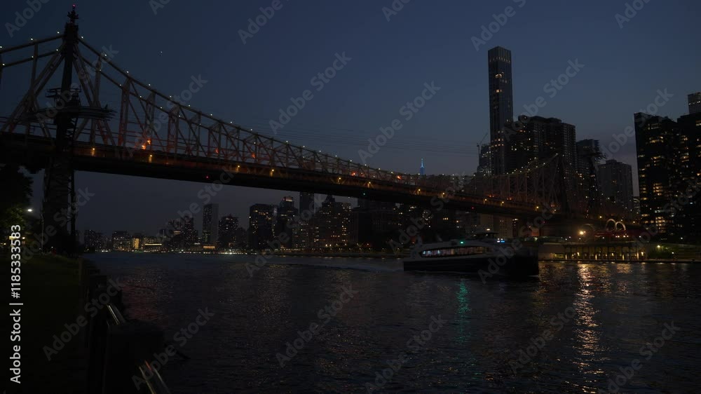 The Queensboro Bridge shines with evening lights as a ferry sails across the East River. The illuminated New York City skyline creates a stunning urban backdrop. The Queensboro Bridge shines with evening lights as a ferry sails across the East River. The illuminated New York City skyline creates a stunning urban backdrop.