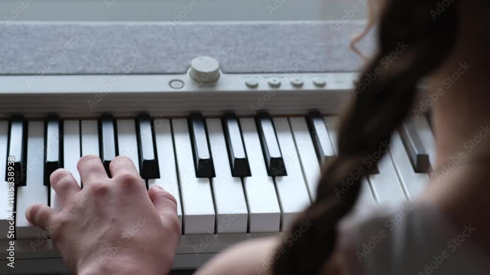 Kid girl playing digital piano at home, over the shoulder view. Child is learning to play an instrument. Focus on keyboard