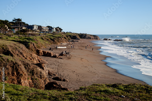 Coastal beach landscape with waves and people enjoying a sunny afternoon near the shoreline. photo