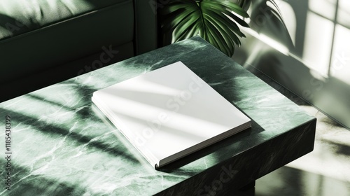 Blank book mockup on green marble coffee table with sunlight and plant.