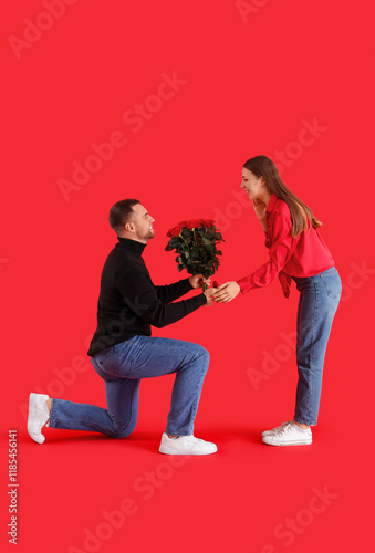 Young man with bouquet of roses proposing to his girlfriend on red background. Valentine's Day celebration photo