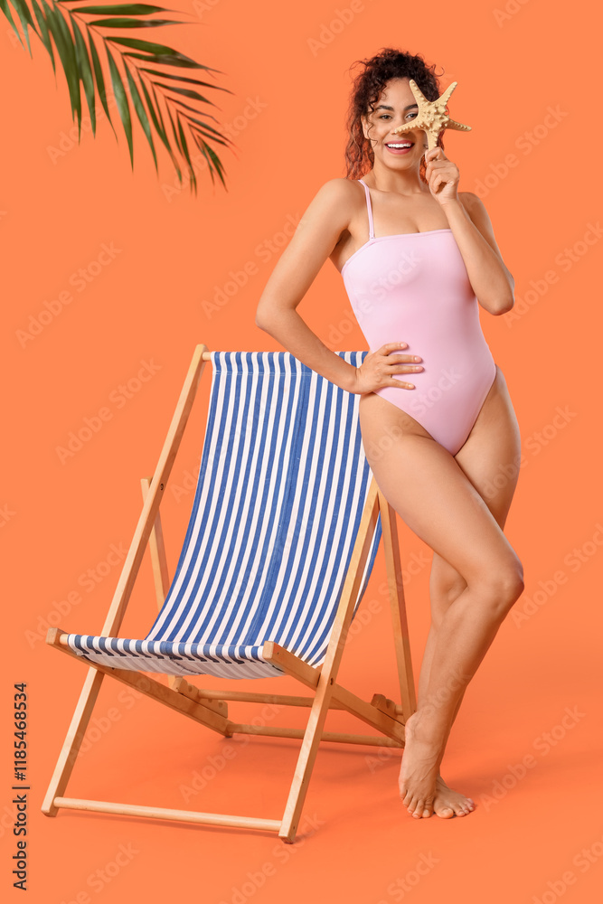 Φωτογραφία Beautiful young African-American woman with starfish and deck chair on orange ba