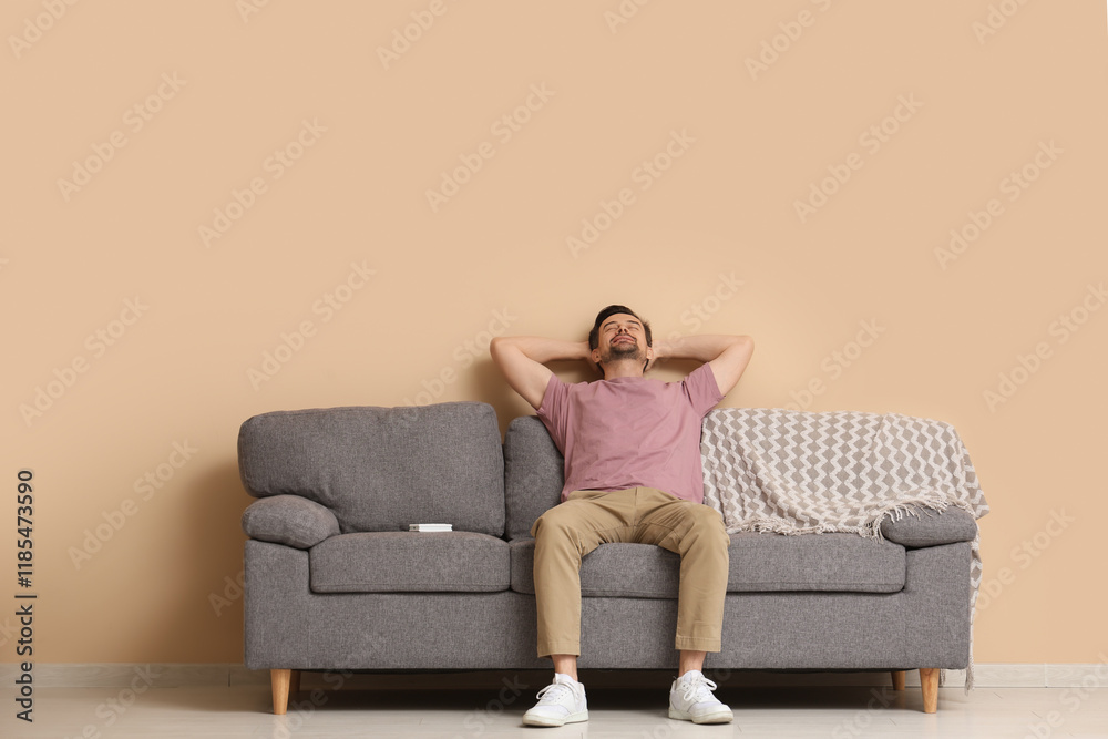 Handsome young man relaxing on sofa with operating air conditioner near beige wall Handsome young man relaxing on sofa with operating air conditioner near beige wall