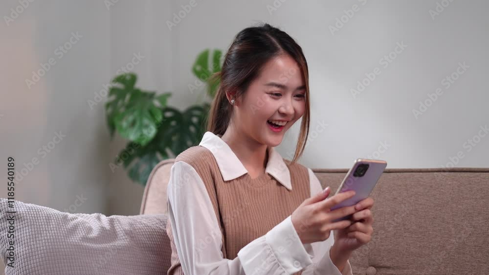 A joyful woman cheering while looking at her smartphone, celebrating good news in a bright living room A joyful woman cheering while looking at her smartphone, celebrating good news in a bright living room