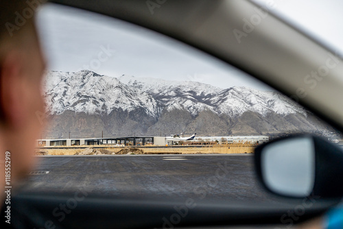 airplane taking off against a backdrop of snow-capped mountains, framed by the interior person driving car window photo