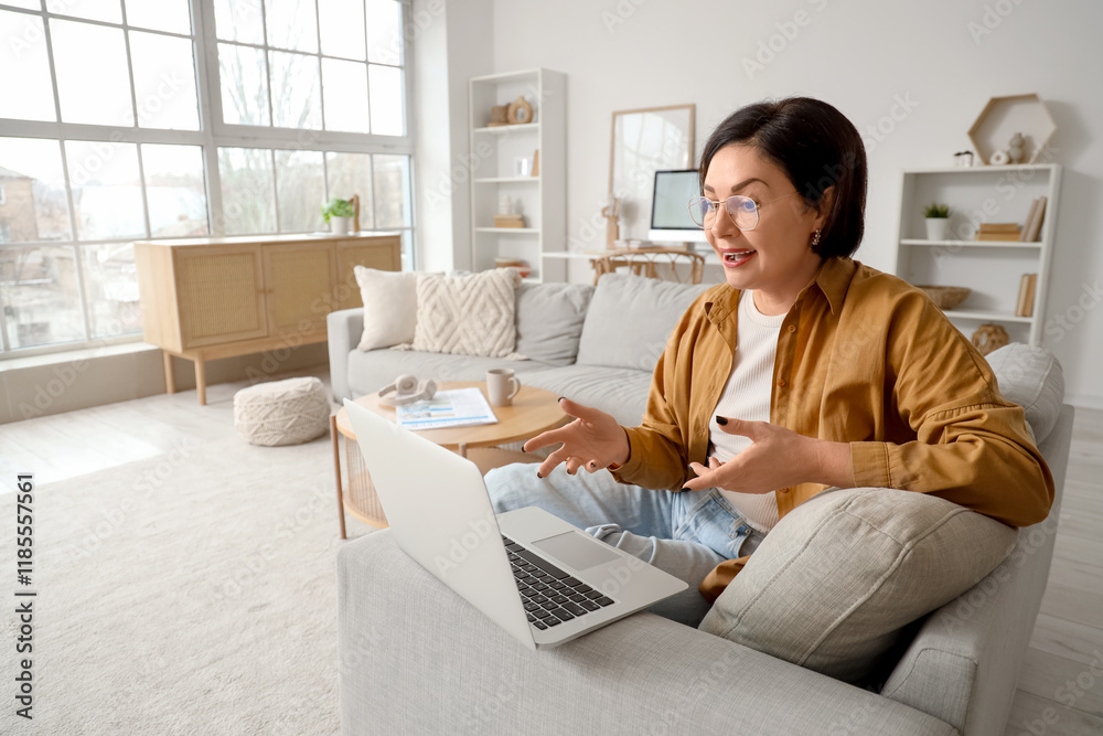 Mature woman with laptop video chatting on couch at home Mature woman with laptop video chatting on couch at home