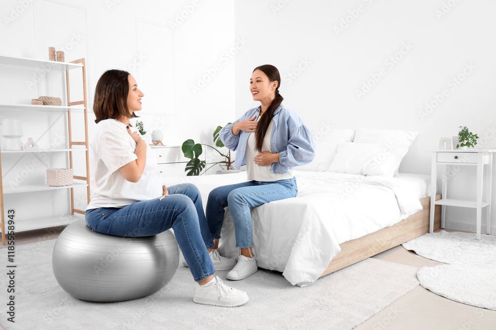 Young Asian doula with pregnant woman training on fitball in bedroom Young Asian doula with pregnant woman training on fitball in bedroom