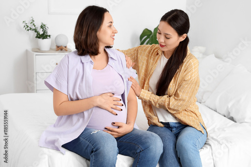 Young Asian doula with pregnant woman sitting in bedroom