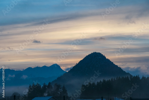 Scenic view of pyramid-shaped conical hill Kathreinkogel surrounded by mountain peaks of Karawanks at sunset. Serene rural landscape in Schiefling am See, Carinthia, Austria. Dramatic sky photo