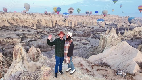 Turkey, Goreme - 26th december, 2024: Couple of travelers having fun wave watching hot air balloons show on viewpoint Cappadocia. Happy friends laughing together on vacation. People xmas trip holidays