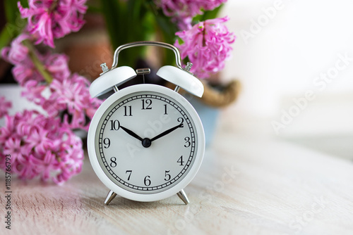 Spring change, Daylight Saving Time concept. White alarm clock and hyacinth flowers on the wooden table. Springtime home gardening, hobby, leisure. Copy space for text