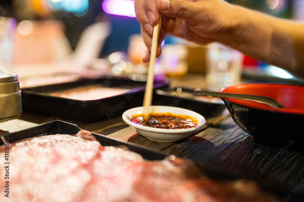 Fototapeta premium Hand man uses wood chopsticks mix and stir the dipping sauce for eating Thai style local hot pot in outdoors restaurant