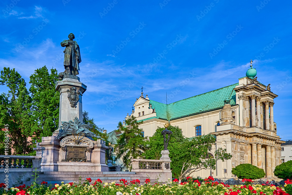 Obraz premium Monument to Adam Mickiewicz in the Adam Mickiewicz Square with colorful red and yellow flowers and blue sky on a summers day, Warsaw, Poland, Europe