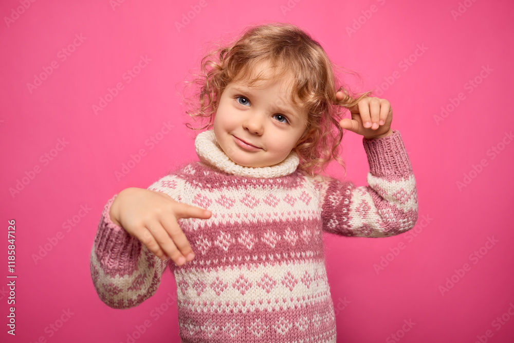 A young girl with curly hair is joyfully posing while twirling a strand of her hair. She wears a cozy sweater with a decorative pattern, creating a cheerful and playful mood A young girl with curly hair is joyfully posing while twirling a strand of her hair. She wears a cozy sweater with a decorative pattern, creating a cheerful and playful mood