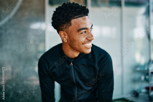 Fit young man in sports clothing laughing while sitting on the floor of a gym during a break from a workout session