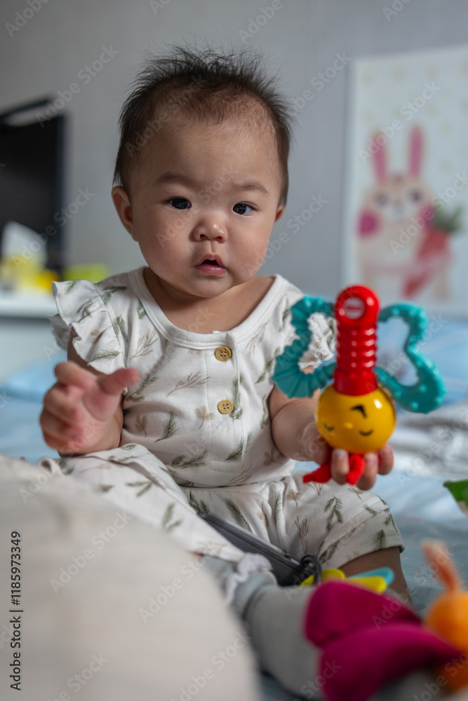 Baby girl is sitting on a bed surrounded by soft toys, playing with a toy in her hand Baby girl is sitting on a bed surrounded by soft toys, playing with a toy in her hand