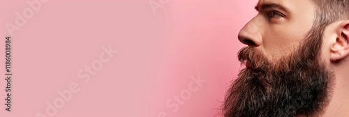 A close-up profile of a man with a well-groomed beard against a soft pink background. Place for text